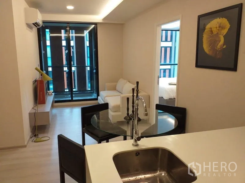 公寓 出租在Khlong Toei, Bangkok - 开放式起居区，白色沙发、落地推拉门通往阳台，带厨房中岛，近BTS通罗的现代公寓。