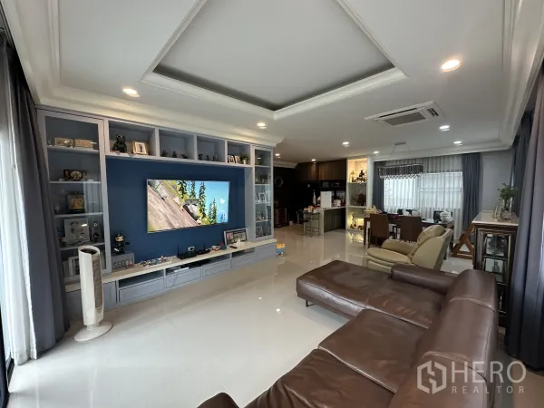 บ้าน ให้เช่าในLam Luk Ka, Pathum Thani - ห้องนั่งเล่นแปลนเปิดพร้อมผนังบิลท์อินทีวีและโซฟาหนังสีน้ำตาล