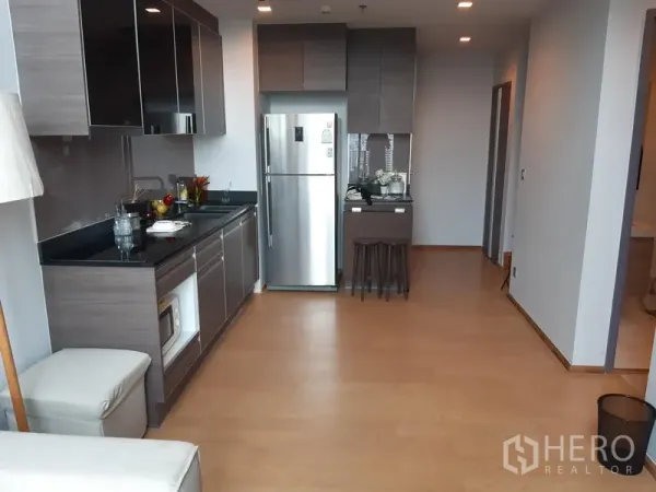 Condominium for rent in Khlong Toei, Bangkok - Open-plan kitchen with grey cabinets, black countertops, and a stainless refrigerator.