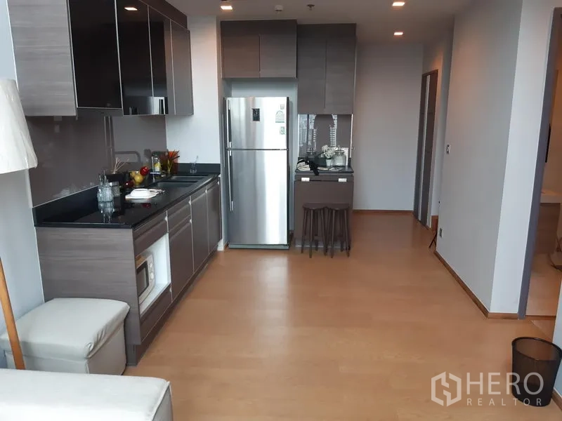 Condominium for rent in Khlong Toei, Bangkok - Open-plan kitchen with grey cabinets, black countertops, and a stainless refrigerator.