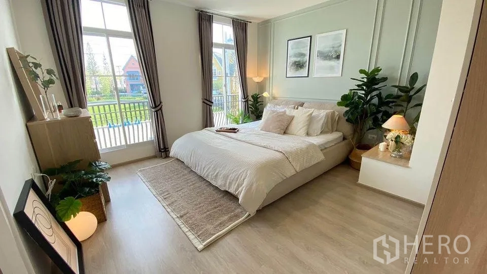 Townhouse for rent in Prawet, Bangkok - Sunlit master bedroom with floor-to-ceiling windows, balcony view and warm wood flooring.