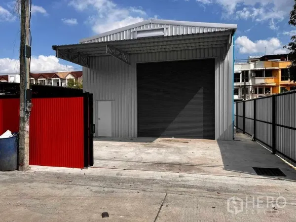 คลังสินค้า ให้เช่าในLat Phrao, Bangkok - โกดังสมัยใหม่ผนังเมทัลชีทในย่านลาดพร้าว พร้อมประตูม้วนขนาดใหญ่ ทางเข้า-ออกมีกำแพงรั้วและลานคอนกรีตสำหรับขนถ่ายสินค้า