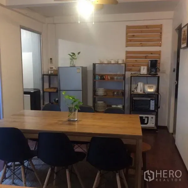 Detached House for rent in Sathon, Bangkok - Dining area with long wooden table, black chairs and an open-shelf kitchenette.