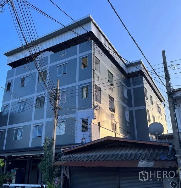 零售空间 出售在Prawet, Bangkok - 临街灰色多层商业楼外立面，金属屋顶与电线杆，傍晚光线下的Prawet街景。