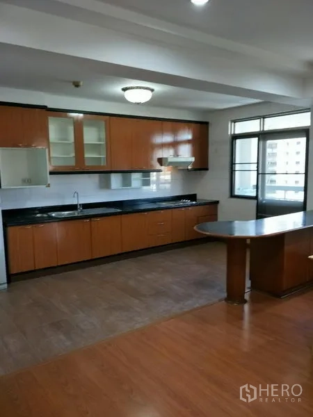 Condominium for rent in Watthana, Bangkok - Full-size kitchen with long black countertops, wooden cabinets, and a breakfast island with bright natural light.
