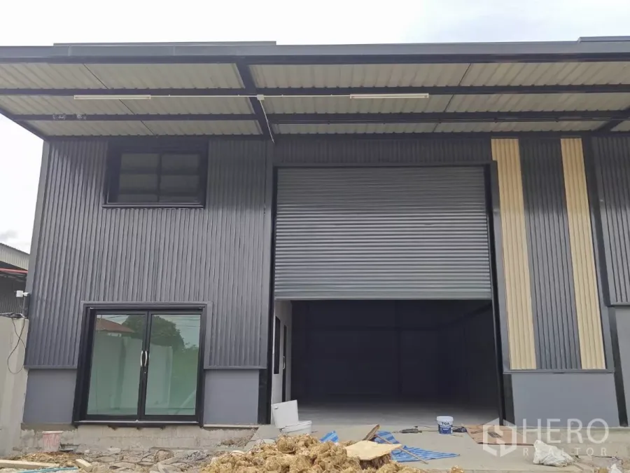 货栈 出租在Sam Phran, Nakhon Pathom - 仓库正面近景，超大卷帘门与玻璃办公室入口