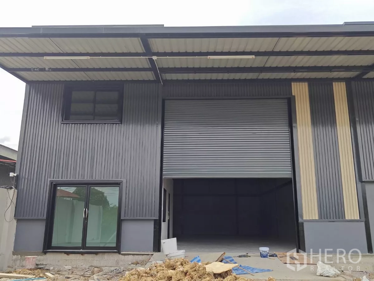 货栈 出租在Sam Phran, Nakhon Pathom - 仓库正面近景，超大卷帘门与玻璃办公室入口