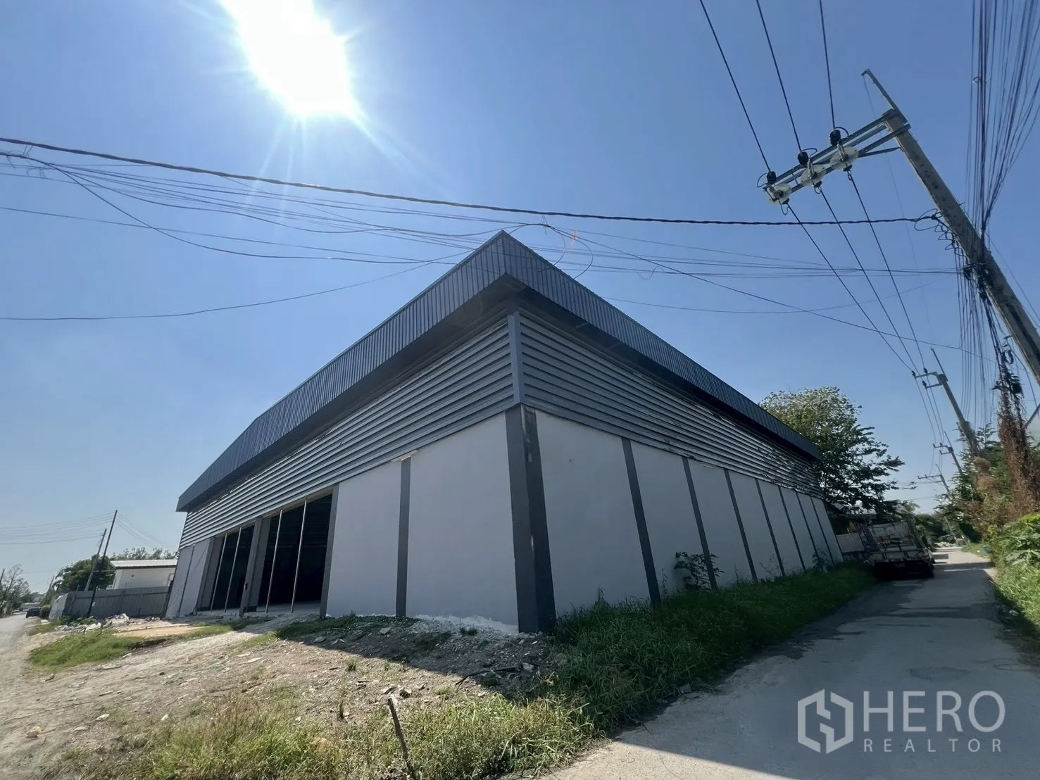 货栈 出租在Bueng Kum, Bangkok - 现代钢结构仓库外观转角视角，金属包板、宽阔门洞，临路出入，晴空阳光充足。