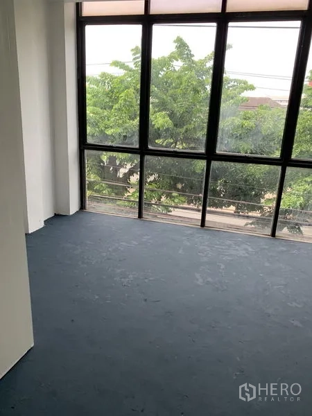 店屋 出租在Bang Na, Bangkok - 落地窗房间，窗外可见绿树与街景。