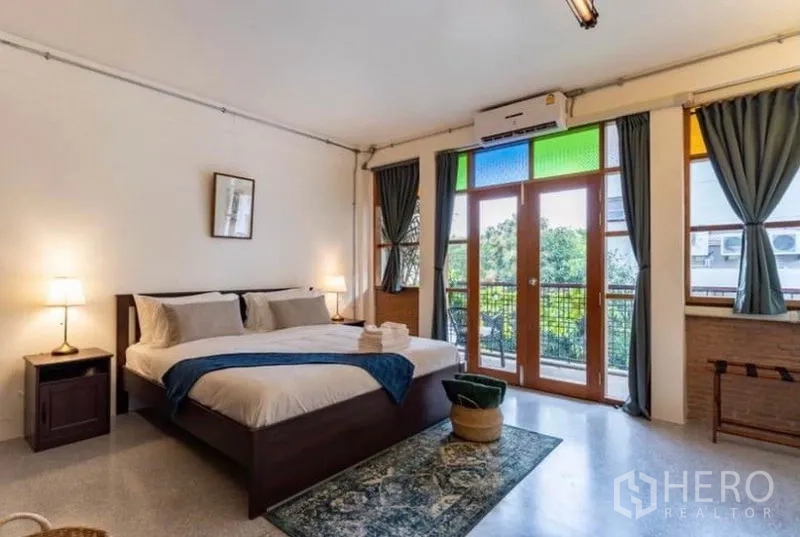 Townhouse for rent in Pathum Wan, Bangkok - Large bedroom with king bed and balcony doors framed by colored glass.