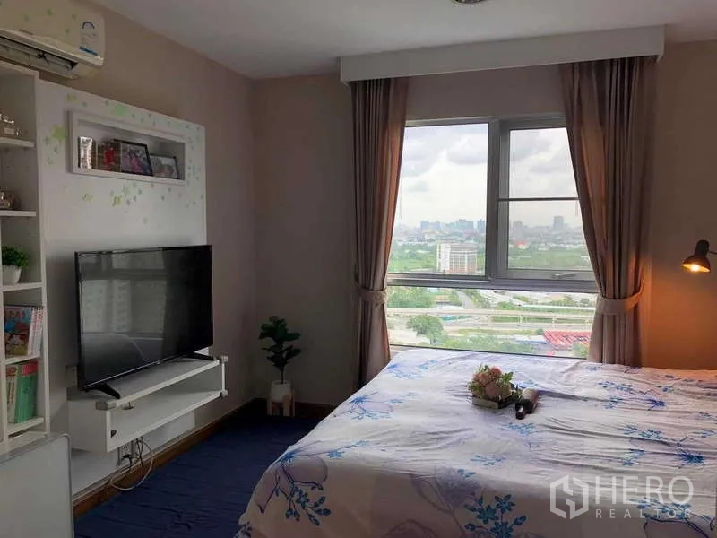 Condominium for sale in Huai Khwang, Bangkok - Master bedroom angle showing panoramic city view through a wide window and TV stand.