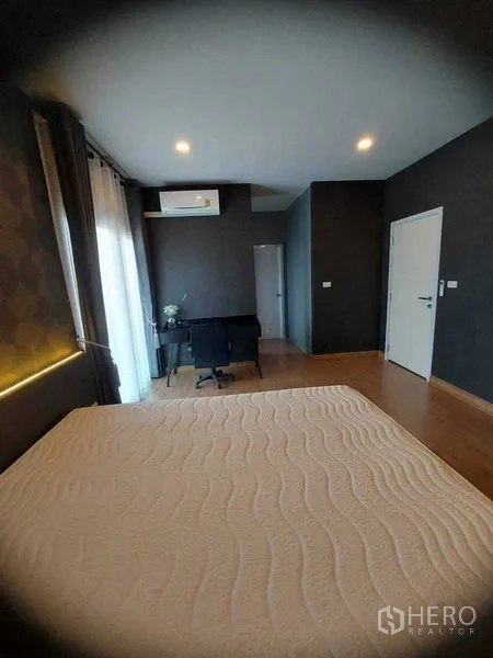 Detached House for rent in Bang Bo, Samut Prakan - Bedroom corner with bed, study desk, air conditioner and balcony curtains.