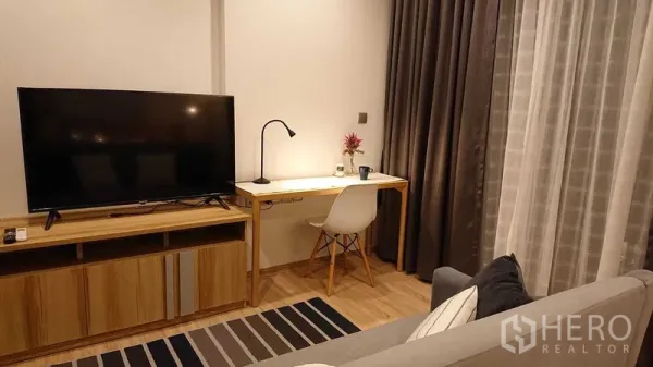 คอนโด ขายในWatthana, Bangkok - ห้องนั่งเล่นสว่างพร้อมชั้นวางทีวี โต๊ะทำงาน พรมลายทาง และผ้าม่านสูงจรดเพดาน ในคอนโดสมัยใหม่ย่านวัฒนา