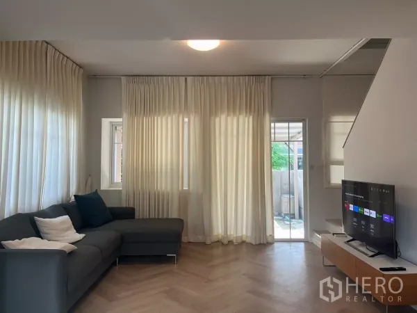 Townhouse for rent in Bang Phli, Samut Prakan - Bright living room with sheer curtains, sliding door, sectional sofa and TV.