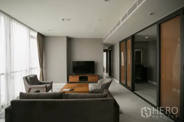 Condominium for rent or sale in Watthana, Bangkok - Bright living area with sheer curtains, long ventilation duct ceiling and hallway leading to bedrooms.