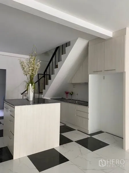 ทาวน์เฮาส์ ให้เช่าหรือขายในKhlong Toei, Bangkok - ครัวสีขาวพร้อมไอส์แลนด์ท็อปสีดำและตู้เก็บของใต้บันได