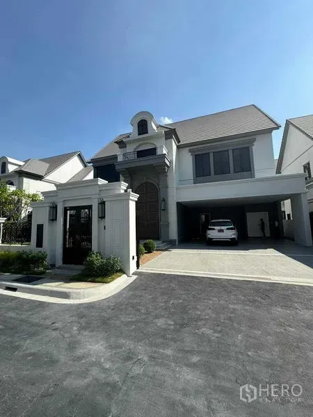 独立式住宅 出租在Bang Khen, Bangkok - 新古典风格两层独栋别墅，带庭院大门、宽阔车道与双车位车棚，蓝天晴朗。