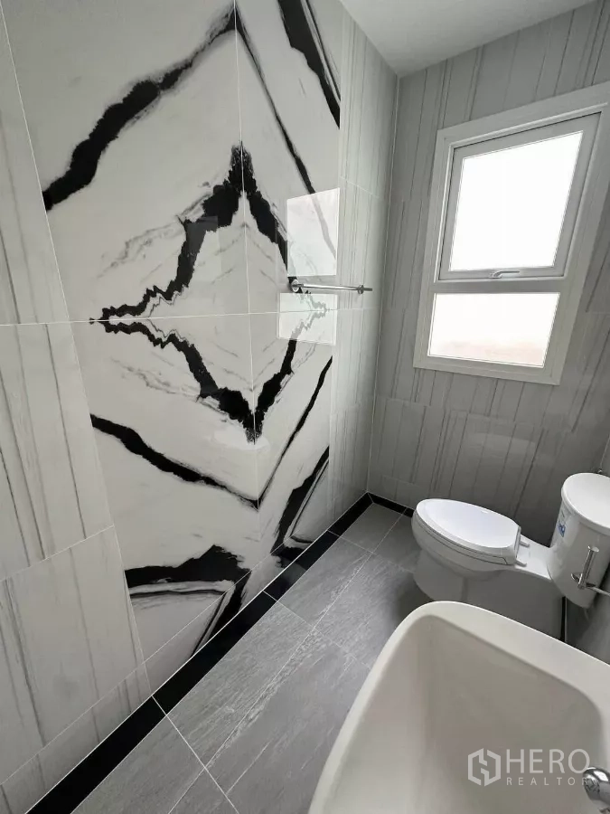 Detached House for rent in Bang Phli, Samut Prakan - Modern bathroom with striking marble-pattern feature wall, window, and sanitary ware.