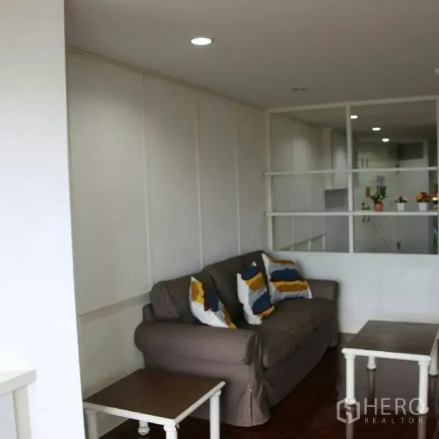 Condominium for rent in Watthana, Bangkok - Bright living room with a gray sofa, colorful cushions, nesting tables, wood floors and a partition to the kitchen.