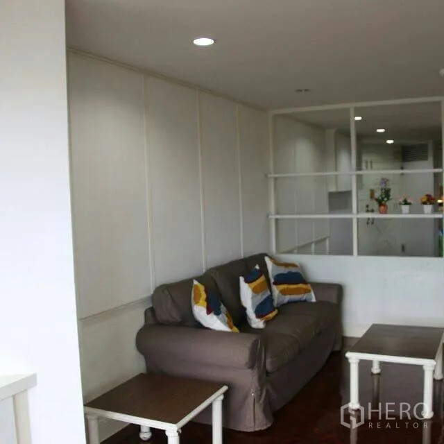 Condominium for rent in Watthana, Bangkok - Bright living room with a gray sofa, colorful cushions, nesting tables, wood floors and a partition to the kitchen.