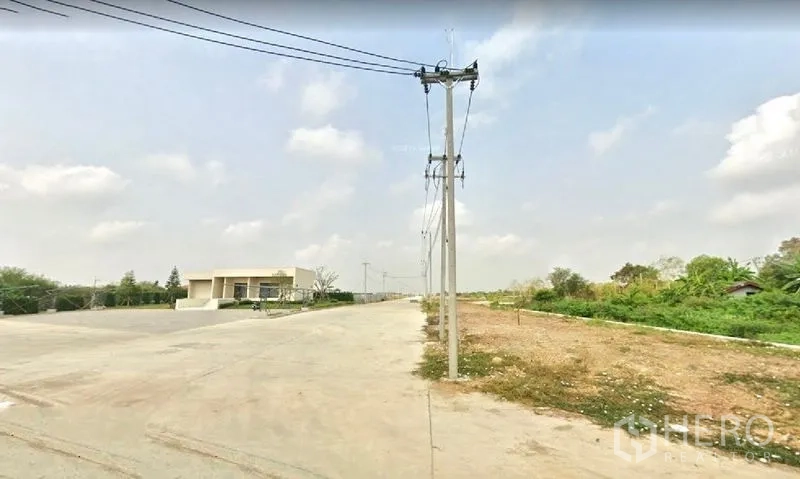 Land for sale in Lam Luk Ka, Pathum Thani - Project entrance area showing a wide turning space, power lines and green verge next to development land.