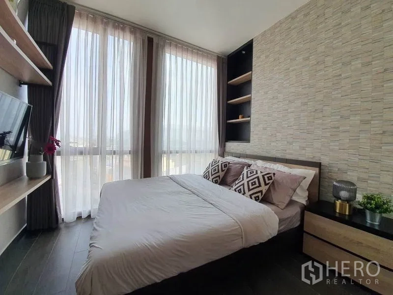 Condominium for rent or sale in Watthana, Bangkok - Second bedroom with bed, wall TV, sheer curtains and textured accent wall.
