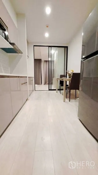 คอนโด ให้เช่าหรือขายในPathum Wan, Bangkok - ครัวแบบแกลเลย์มองไปยังฉากกั้นกระจกและโต๊ะกินข้าว พื้นไม้ทั่วทั้งห้อง