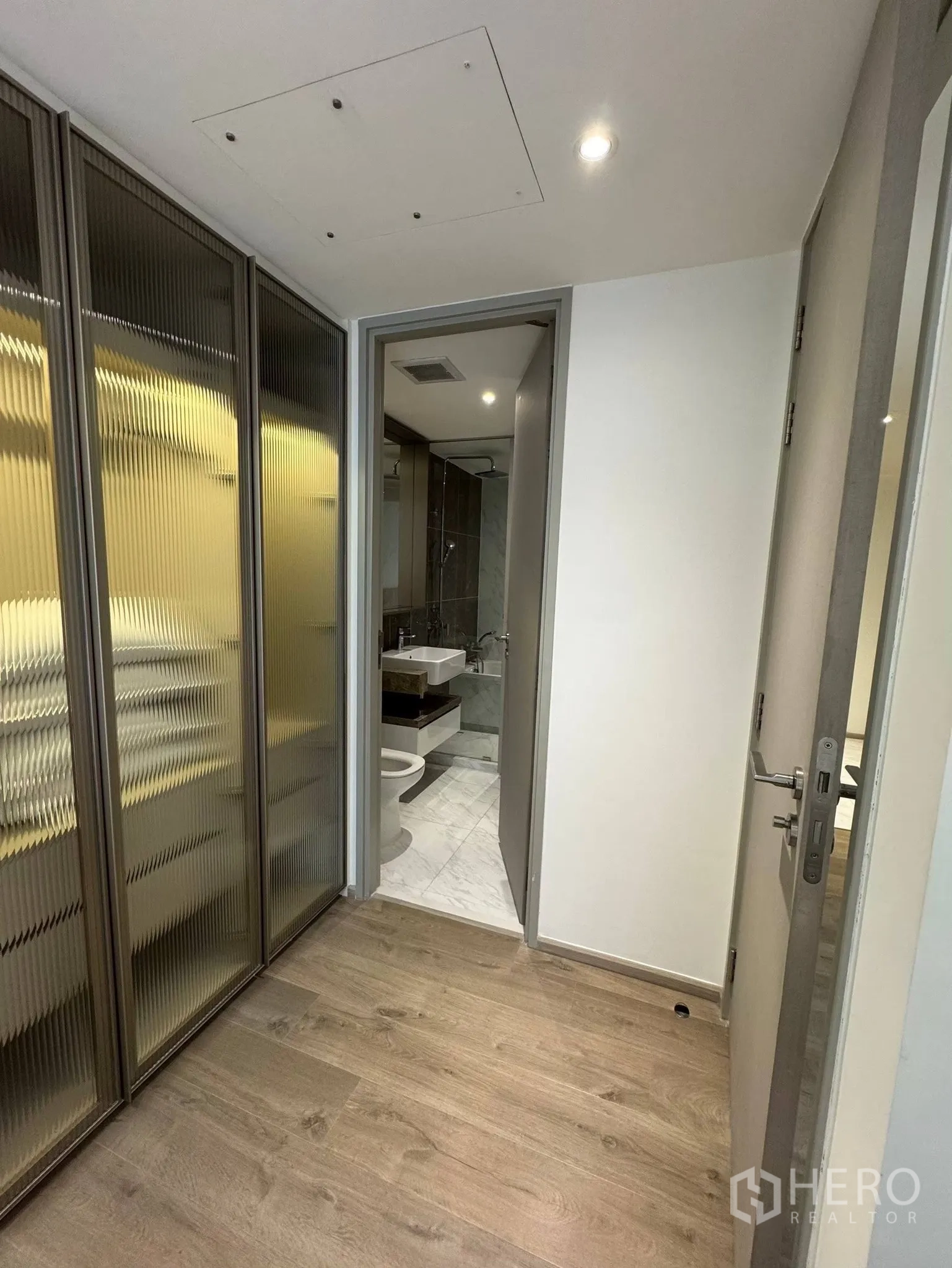 Condominium for rent in Khlong Toei, Bangkok - Hallway with fluted-glass built-in wardrobe leading to a marble-tiled bathroom.