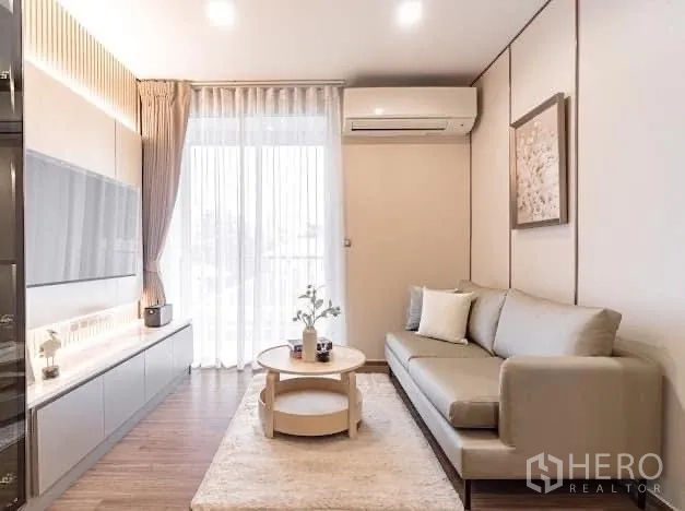 Condominium for rent in Watthana, Bangkok - Light-filled living room with sofa, TV wall and balcony curtain.