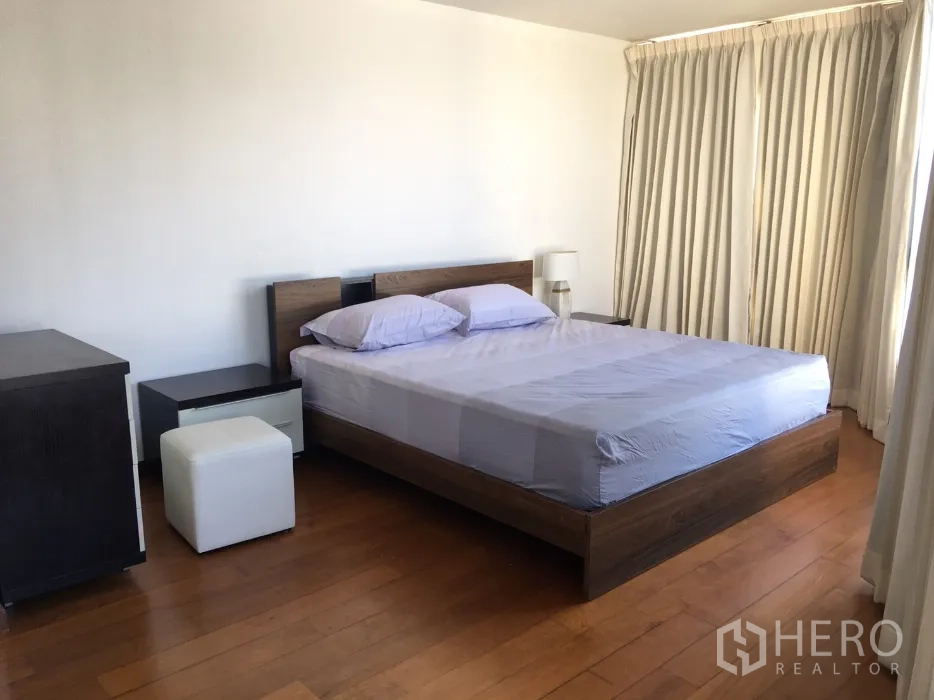 Condominium for rent or sale in Watthana, Bangkok - Large bedroom with double bed, side tables, wood flooring and full-height curtains.