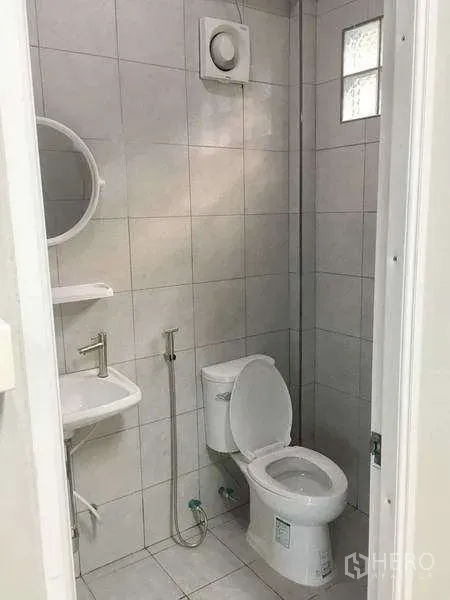 Warehouse for rent in Mueang Samut Prakan, Samut Prakan - Compact tiled restroom with toilet, sink, mirror, and exhaust fan.