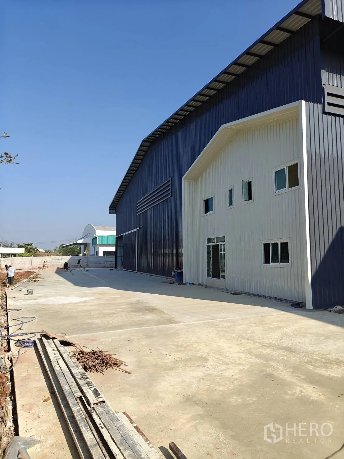 Factory for rent in Mueang Samut Sakhon, Samut Sakhon - Exterior perspective of the factory and office wing with a wide concrete yard suitable for truck maneuvering.