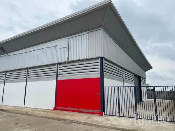 Warehouse for rent or sale in Sai Noi, Nonthaburi - Street-side facade of warehouse with red panel and tall metal fence gate.