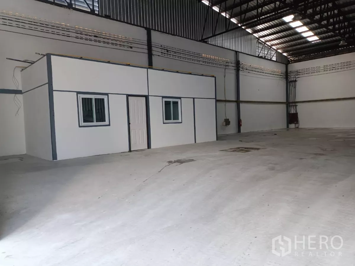 Warehouse for rent in Suan Luang, Bangkok - Spacious warehouse interior with concrete floor and a built-in office box featuring windows and a door.