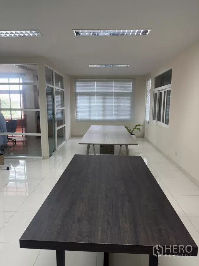 Factory for sale in Lam Luk Ka, Pathum Thani - Bright open-plan office with long worktables, window blinds and a glass-partitioned room.
