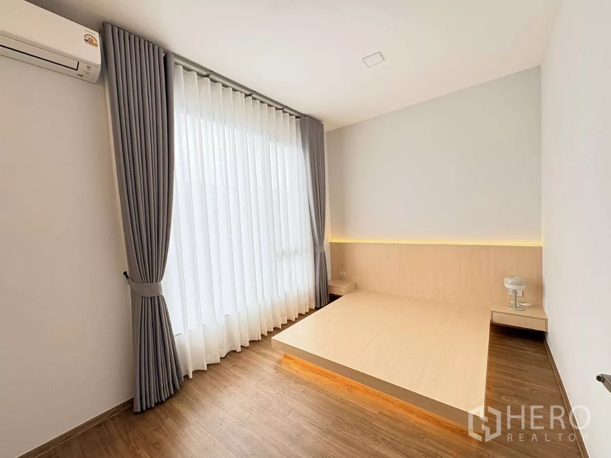 Townhouse for rent in Bang Phli, Samut Prakan - Bedroom with platform bed, grey curtains and wall-mounted air conditioner.