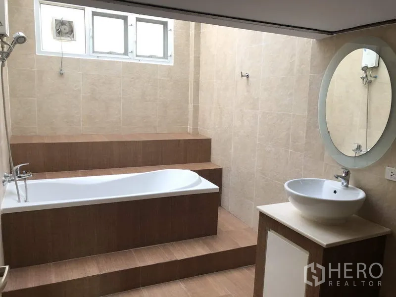 Detached House for rent in Suan Luang, Bangkok - Bathroom with step-up bathtub, beige tiles, vanity and round mirror