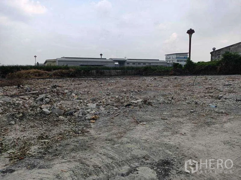 Land for rent in Lat Krabang, Bangkok - Cleared gravel land parcel with factory buildings in the background within an industrial zone.