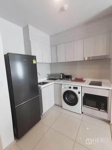 Condominium for rent in Pathum Wan, Bangkok - Modern compact kitchen with black refrigerator, washer, microwave and cooktop.