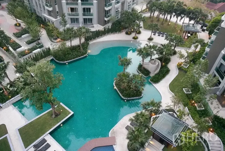 Condominium for rent in Huai Khwang, Bangkok - Aerial view of a resort-style condominium swimming pool surrounded by lush gardens and pathways.