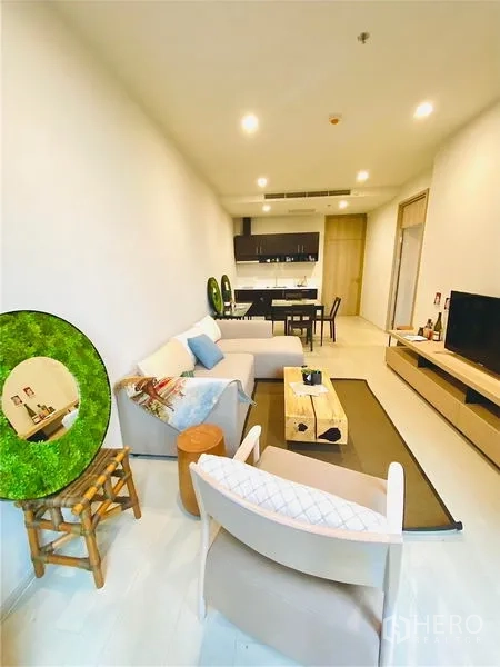 คอนโด ให้เช่าในPathum Wan, Bangkok - วิวนั่งเล่นไปยังครัวแบบเปิดและผนังทีวี โทนสีอบอุ่นและไฟดาวน์ไลท์