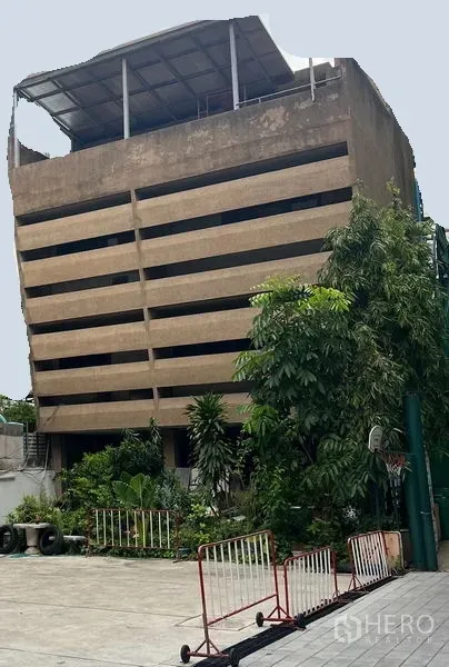 零售空间 出租在Khlong Toei, Bangkok - 多层混凝土建筑，水平百叶式立面，屋顶遮棚，一层前院有绿植与围栏，位于曼谷空堤区。