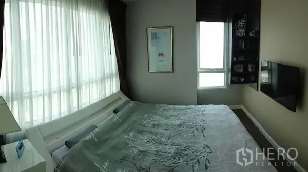 Condominium for rent or sale in Watthana, Bangkok - Bright corner bedroom with floor-to-ceiling window, wall-mounted TV and built-in shelves.