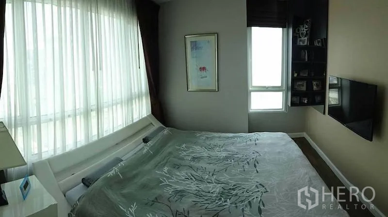 Condominium for rent or sale in Watthana, Bangkok - Bright corner bedroom with floor-to-ceiling window, wall-mounted TV and built-in shelves.