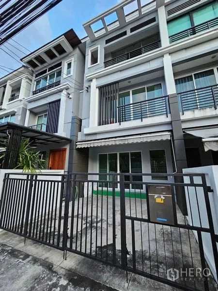 Townhouse for rent in Wang Thonglang, Bangkok - Modern three-storey townhouse facade with balconies, sliding glass doors, and gated carport.