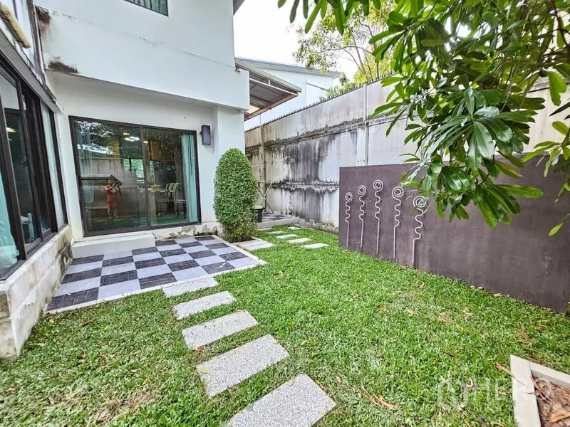 Detached House for sale in Prawet, Bangkok - Backyard with small patio of chequer tiles, sliding doors, stepping‑stone path and grass lawn.