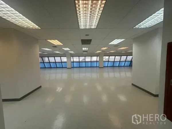 สำนักงาน ให้เช่าในPhaya Thai, Bangkok - สำนักงานแบบโอเพ่นสเปซ มีหน้าต่างกระจกเอียงโทนฟ้าตลอดแนว และไฟเพดานสว่างทั่วห้อง.