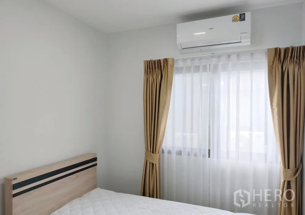Townhouse for rent in Bang Phli, Samut Prakan - Bedroom with bed, curtains and a wall-mounted air conditioner above the window.
