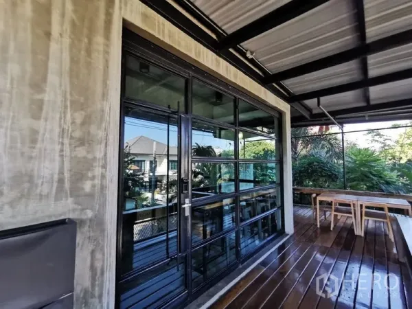 Home Office for sale in Wang Thonglang, Bangkok - Covered wooden terrace with black-framed glass doors and bench seating overlooking greenery.