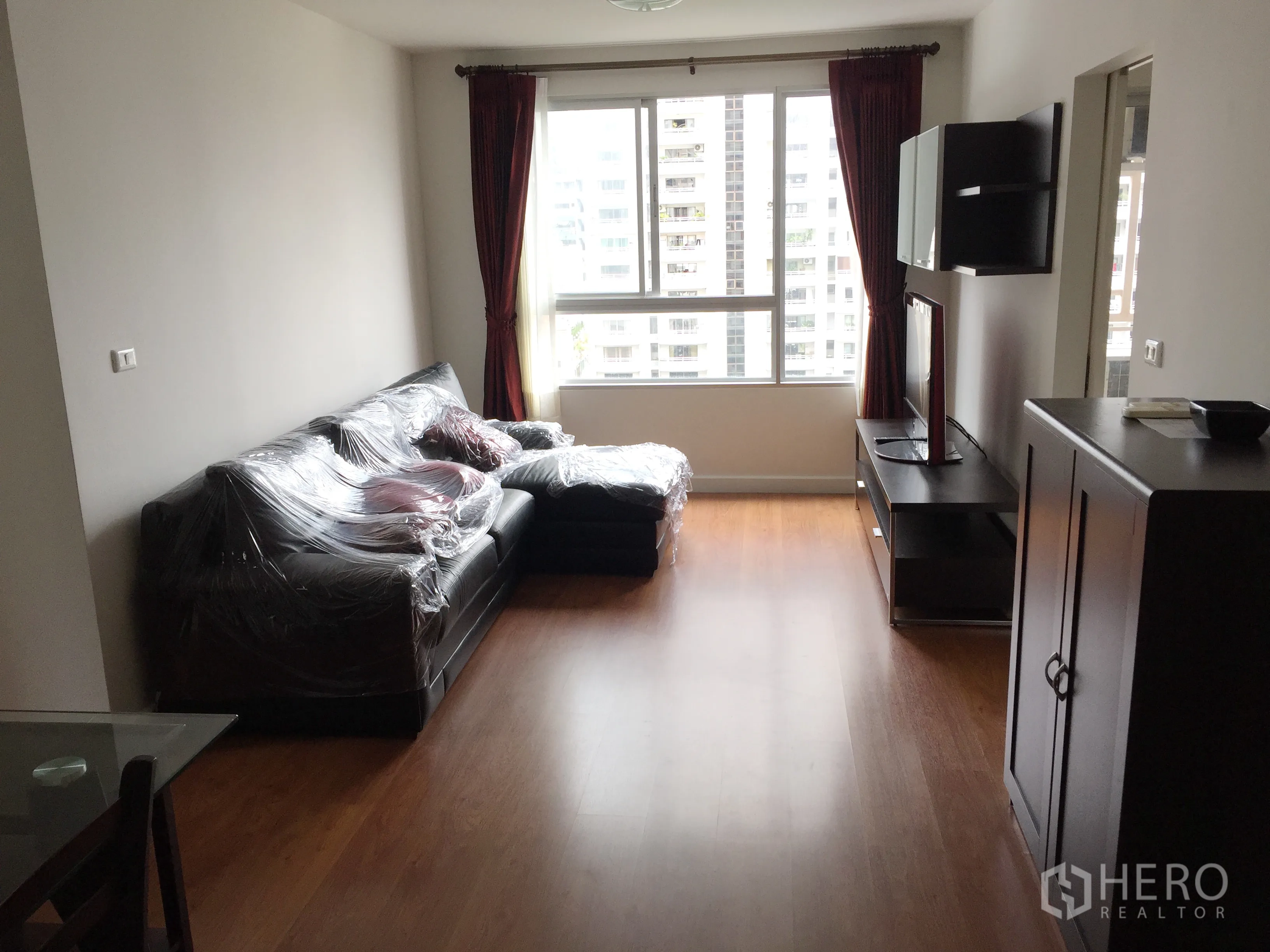 คอนโด ให้เช่าในKhlong Toei, Bangkok - ห้องนั่งเล่นสว่าง พื้นไม้ โซฟารูปตัวแอล ตู้ทีวี และหน้าต่างวิวเมือง